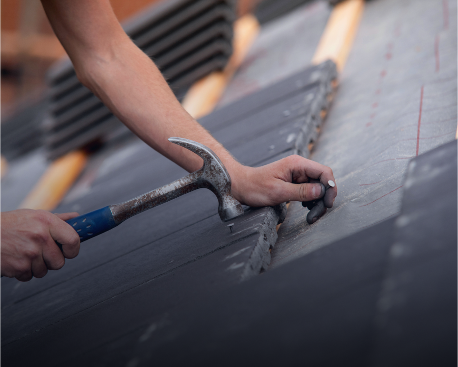 Roofer hammering nails into roof tiles.