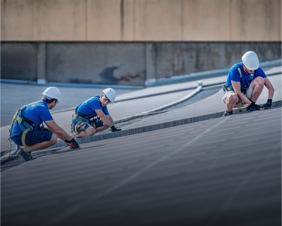 Workers in safety gear on sloped roof.