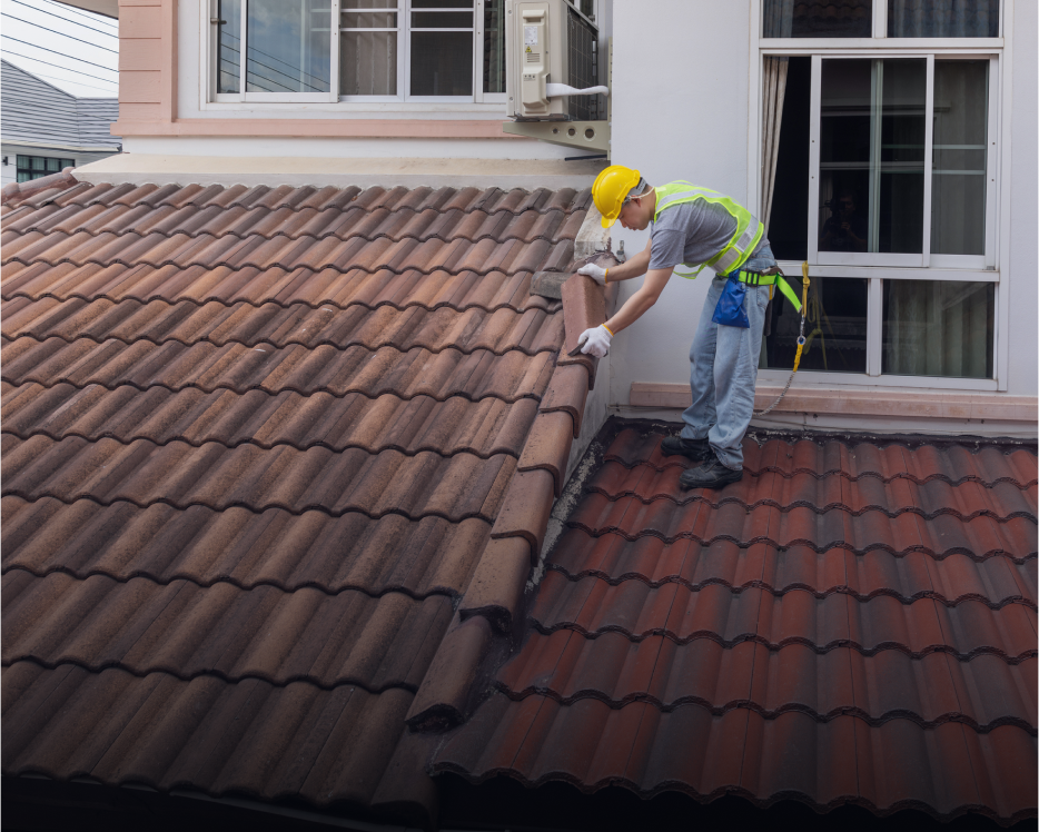 Worker inspecting roof tiles on ladder.