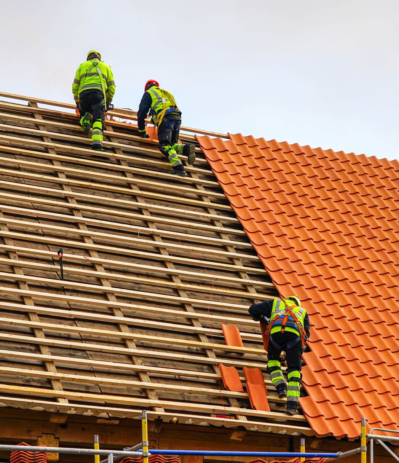 Roofers installing orange tiles on rooftop.