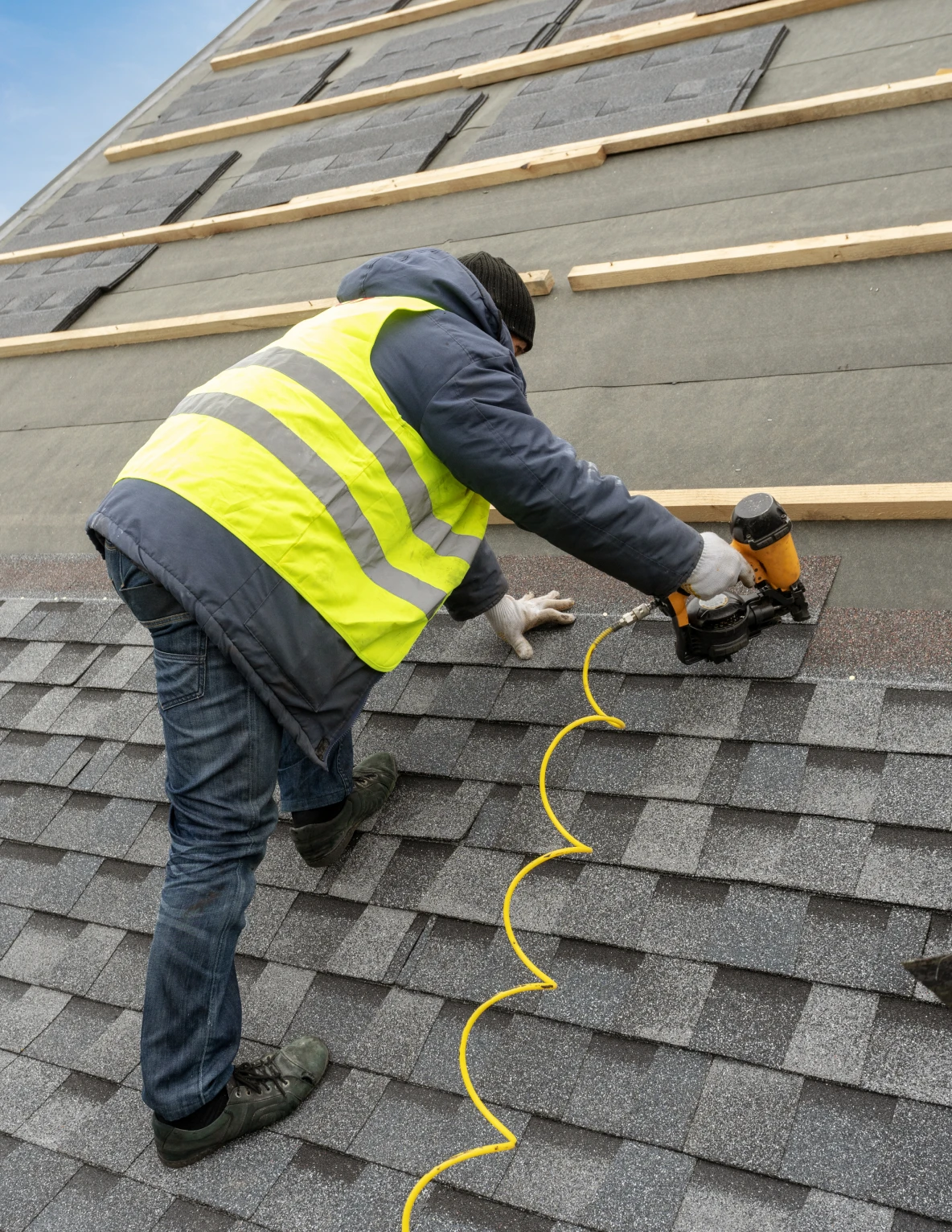 Roofer installing shingles with nail gun.