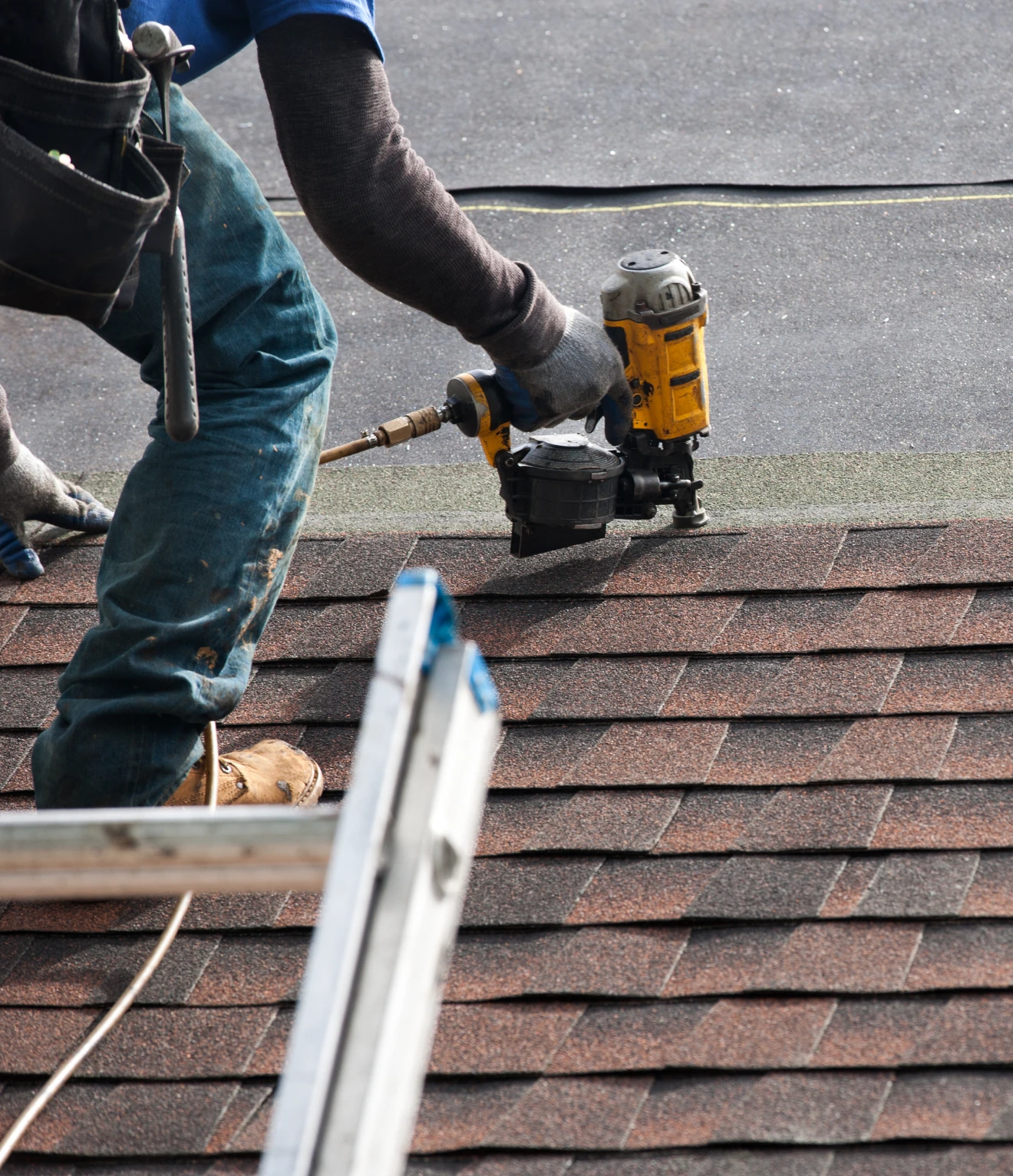 Worker using nail gun on roof shingles.